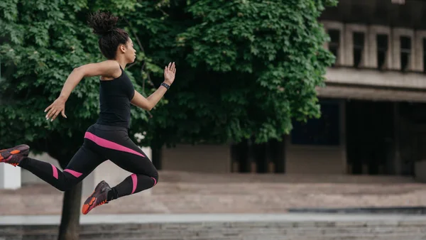 Sağlıklı yaşam tarzı ve vücut enerjisi. Afrikalı Afro-Amerikalı spor elbiseli kız atlayışta havada dondu, şehirde koşuyor. — Stok fotoğraf