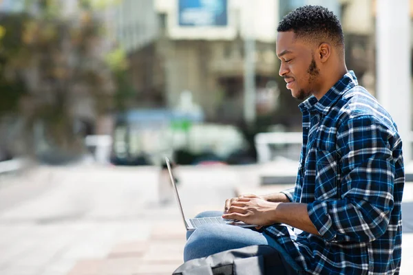 Μαύρος που χρησιμοποιεί φορητό υπολογιστή, κάθεται στο κέντρο με gadget — Φωτογραφία Αρχείου