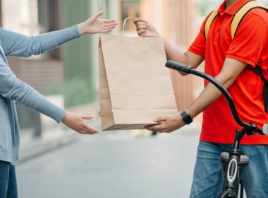 Bisikletli kuryeyle online alışveriş ve teslimat. Sırt çantalı adam müşteriye kese kağıdı veriyor.