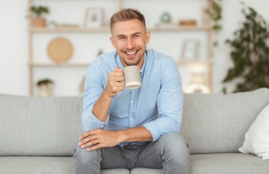 Genç adam kahve içiyor ve kameraya poz veriyor.