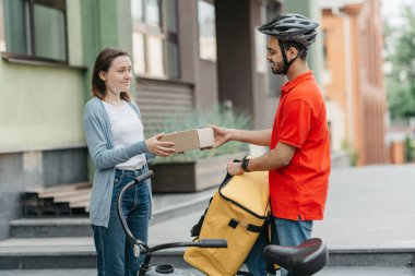 Memnun müşteri çevrimiçi sipariş alıyor. Kız sırt çantalı ve bisikletli kuryeden karton paket alıyor.