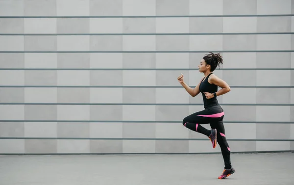 Corredor en pista después del entrenamiento. Chica afroamericana en ropa deportiva y con rastreador de fitness, trotando — Foto de Stock