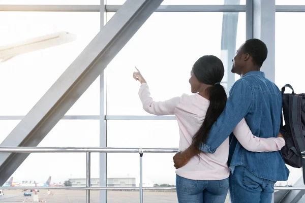 Excited african couple looking at plane departure from window in airport — Stock Photo, Image