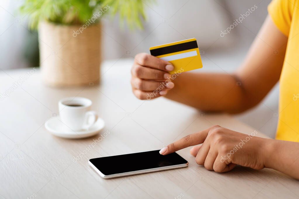 Black woman using phone and credit card at home