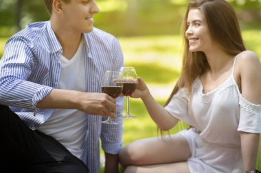 Parkta kırmızı şarap içen genç çift, içkili bardaklara odaklan.