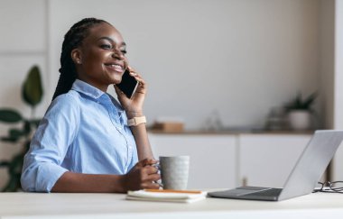 İşte rahatla. Mutlu siyah sekreter cep telefonuyla konuşuyor ve kahve içiyor.