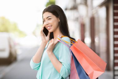 Tüketim kavramı. Alışveriş torbaları taşıyan ve dışarıda cep telefonuyla konuşan Asyalı kız.