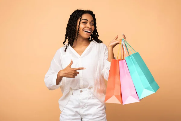 Africano shopaholic ragazza mostra shopper borse in piedi oltre beige sfondo — Foto Stock
