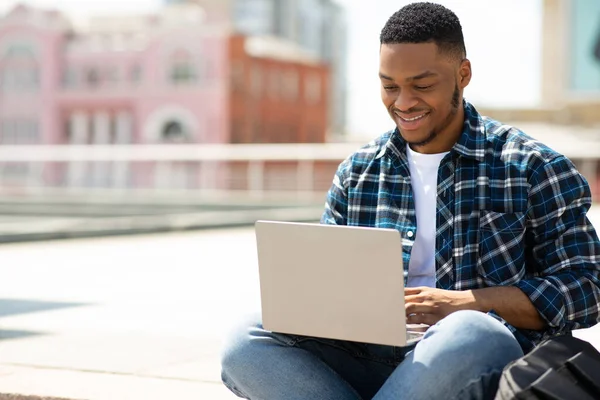 Homem negro feliz usando laptop, sentado no centro da cidade — Fotografia de Stock