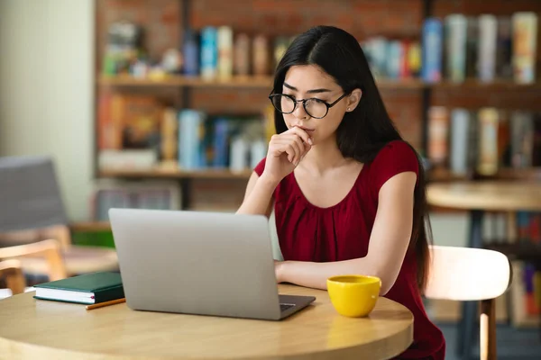 Focado asiático menina estudante em óculos estudando on-line com laptop no café — Fotografia de Stock