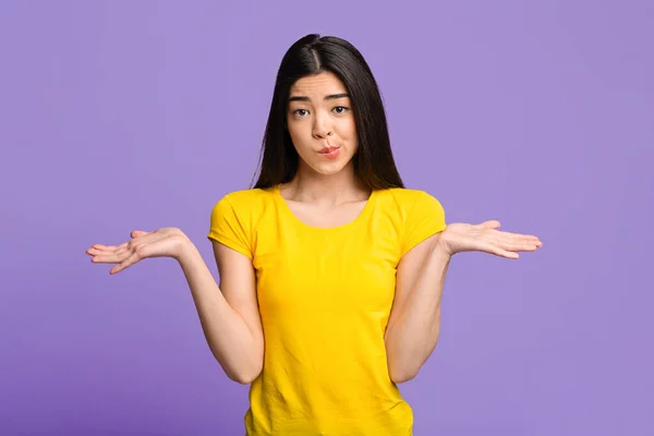 Ich weiß es nicht. Unachtsames asiatisches Mädchen zuckt mit den Schultern über lila Studiohintergrund — Stockfoto