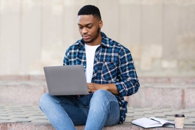 Öğrenci dizüstü bilgisayar kullanıyor, şehirde sınırda oturuyor.