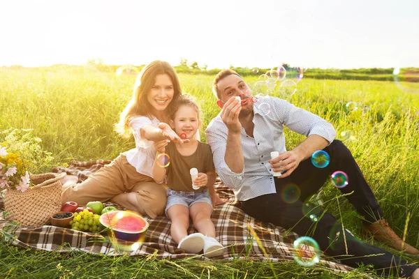 Linda família soprando bolhas de sabão em um piquenique no prado — Fotografia de Stock