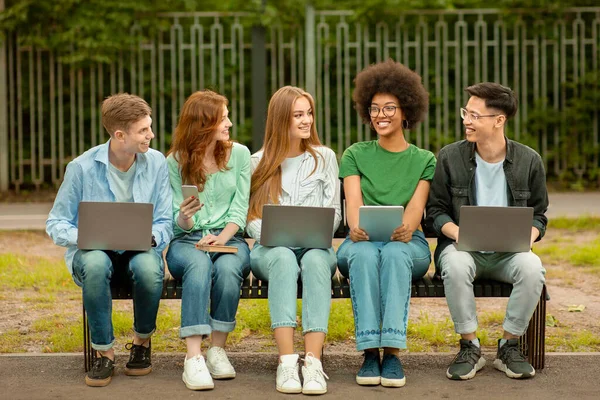 Projekt grupowy. Wielorasowi studenci studiów na świeżym powietrzu z laptopami i tabletem cyfrowym — Zdjęcie stockowe