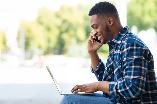 Μαύρος που χρησιμοποιεί φορητό υπολογιστή, κάθεται στην πόλη με κινητό τηλέφωνο — Φωτογραφία Αρχείου