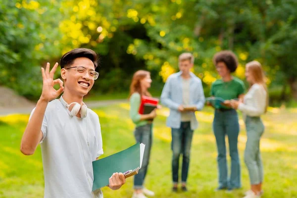 Chico estudiante chino feliz gestos bien mientras posando al aire libre en el campus — Foto de Stock