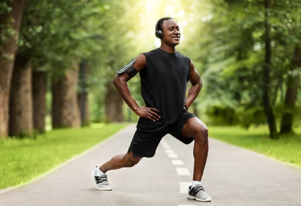 Glücklicher afrikanischer Sportler streckt die Beine, trainiert im Park — Stockfoto