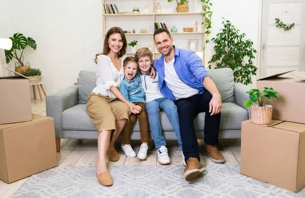 Vreugdevolle familie van vier zitten op de bank na verhuizing binnen — Stockfoto