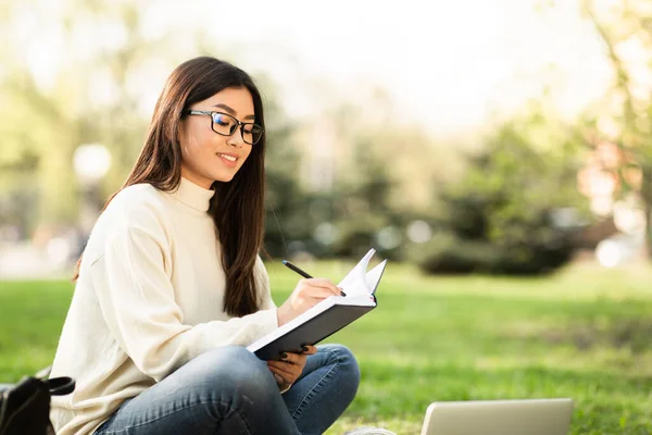 Chica escribiendo en el diario, sentado en el parque moderno — Foto de Stock