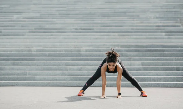 Esneklik egzersizleri. Spor kıyafetli neşeli Afro-Amerikalı kız spor ayakkabıları ve spor ayakkabıları ile geriniyor. — Stok fotoğraf