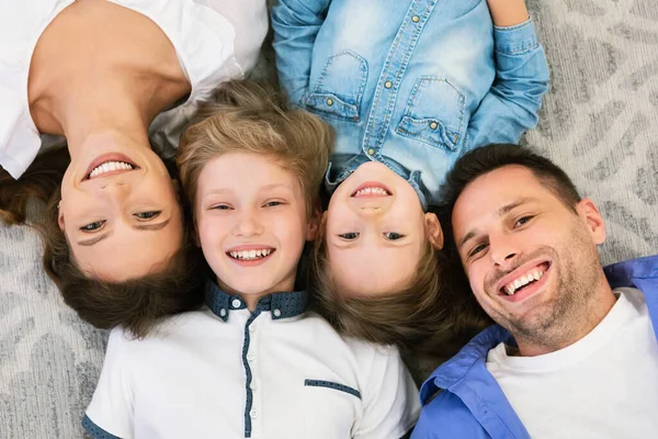 Sorrindo pais e filhos deitados no chão posando dentro de casa, acima da vista — Fotografia de Stock