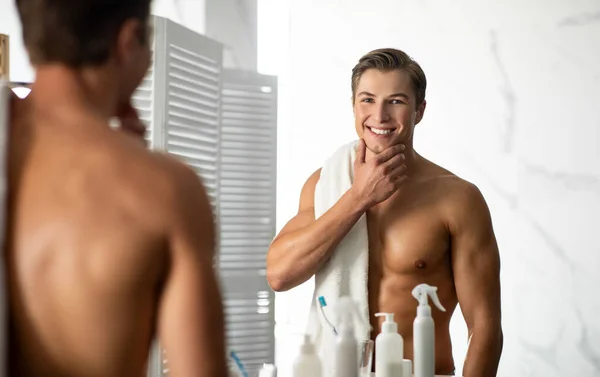 Selbstbewusster junger Mann blickt in den Spiegel, berührt Kinn — Stockfoto