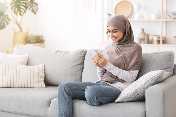 Modern Muslim Girl Menggunakan Smartphone At Home While Relaxing On Couch — Stok Foto