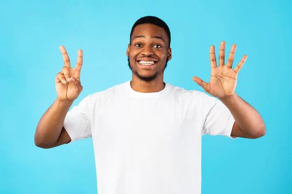 Hombre negro mostrando número siete sonriendo a la cámara, fondo azul — Foto de Stock