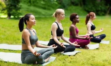 Bir grup milenyum kızı parkta yoga meditasyon dersine katılıyor.