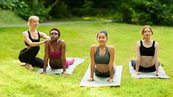 Учитель йоги помогает девочкам тысячелетия правильно позировать во время занятий на открытом воздухе в парке — стоковое фото