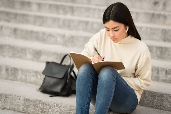 Menina escrevendo no diário, sentado nas escadas cinza — Fotografia de Stock