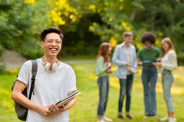 Portrait Of Happy Asian Student Guy With Workbooks And Backpack Posing Outdoors clipart