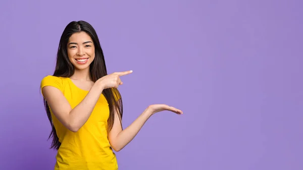 Tolles Angebot. Freudiges asiatisches Mädchen zeigt auf unsichtbares Objekt auf ihrer Handfläche — Stockfoto