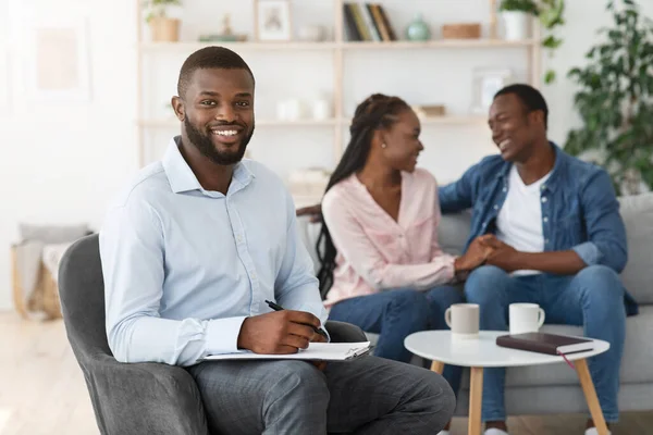 Succesvolle therapie. glimlachende adviseur poseren met terwijl gelukkig zwarte echtgenoten op de achtergrond — Stockfoto