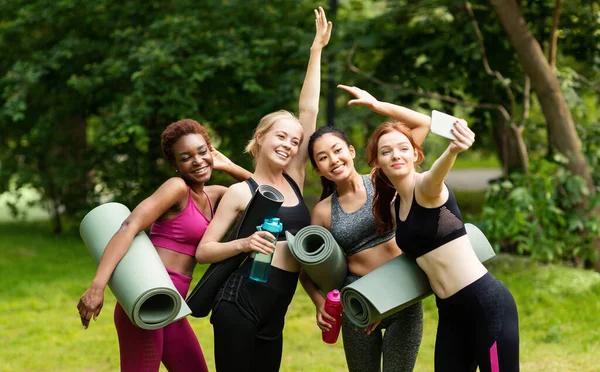 Meninas multirraciais alegres em roupas esportivas tomando selfie antes de sua prática de ioga ao ar livre — Fotografia de Stock