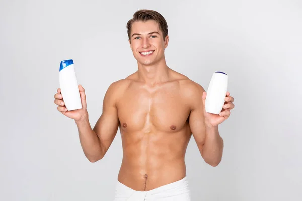 Bello ragazzo sorridente in piedi con shampoo in mano — Foto Stock