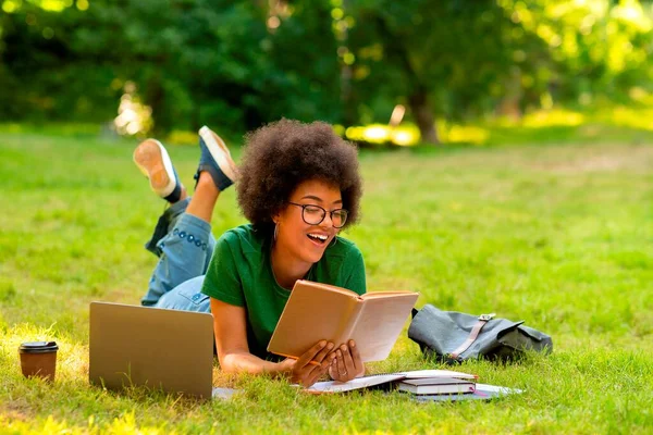 快乐的非洲女学生在户外看书，躺在公园的草坪上 — 图库照片