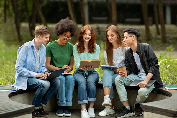 Wielokulturowi studenci studiujący na świeżym powietrzu z książkami i urządzeniami, przygotowujący się do lekcji — Zdjęcie stockowe