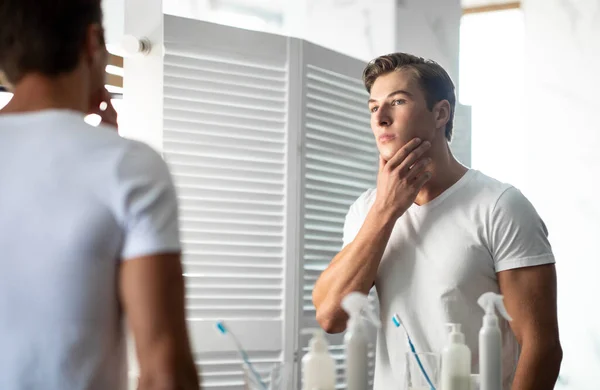 Stilig ung man tittar i spegeln, rör vid hakan — Stockfoto