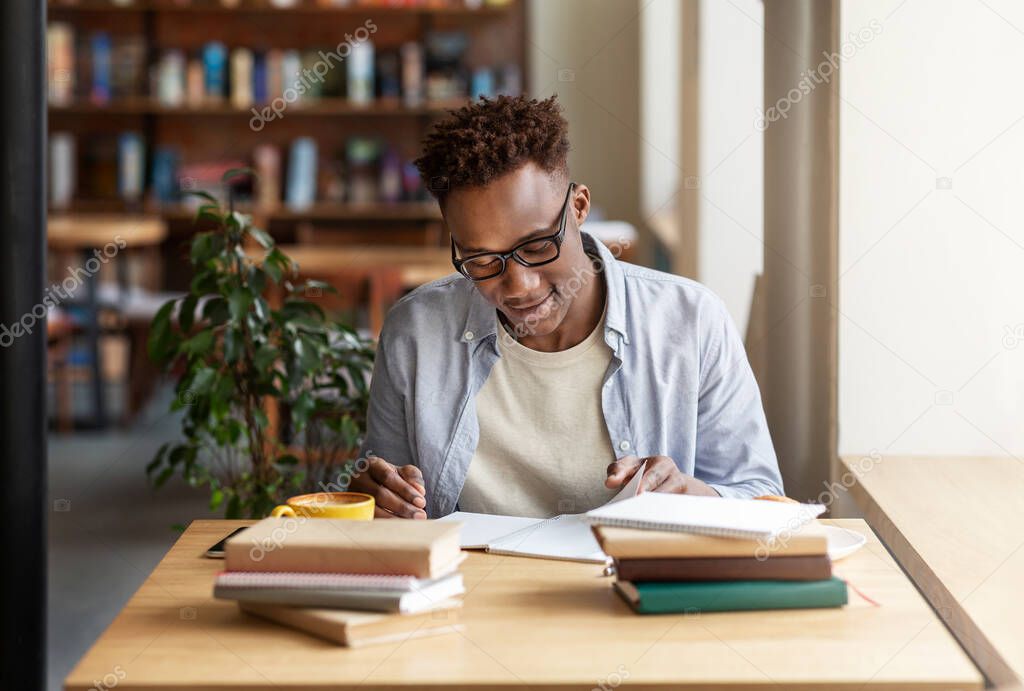 Happy black guy studying or working with books at coffee shop