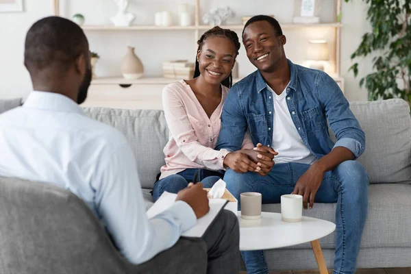 Skuteczna terapia małżeńska. Szczęśliwa afrykańska para siedzi na kanapie w biurze doradców — Zdjęcie stockowe