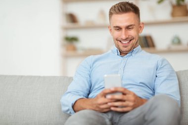 Evde akıllı telefon kullanan neşeli yetişkin bir adam.