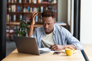 Sinirli Afro-Amerikalı adam şehir kafesinde zor bir iş projesi için dizüstü bilgisayar kullanıyor.