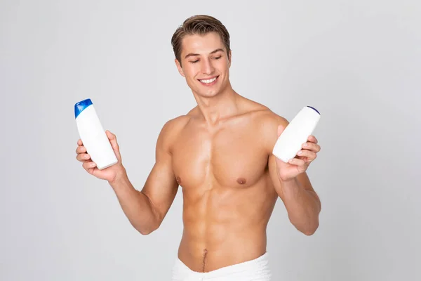 Schöner junger Kerl steht mit Shampoo in den Händen — Stockfoto