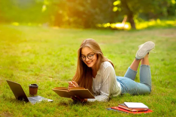 Привлекательная девушка в очках, читающая книгу на открытом воздухе, наслаждающаяся учебой в парке — стоковое фото
