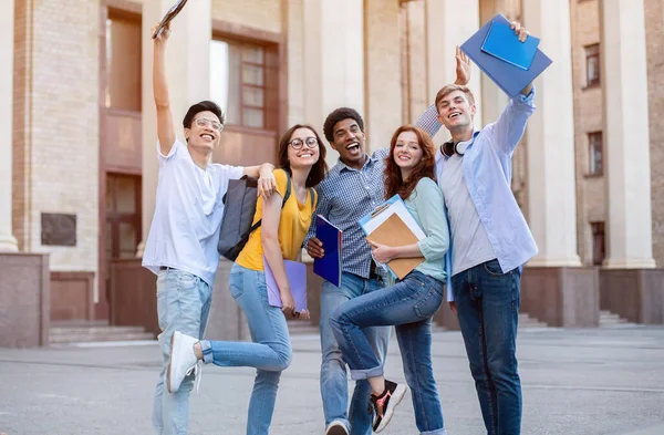 Estudantes multirraciais levantando mãos e livros no ar — Fotografia de Stock