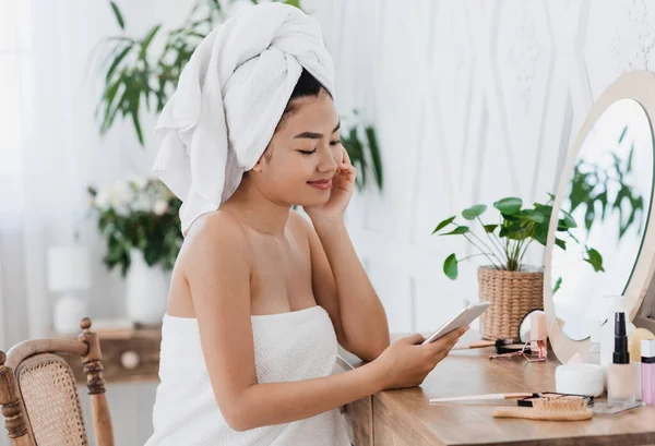 Ασιάτισσα με πετσέτα χρησιμοποιώντας smartphone, διαβάζοντας το blog ομορφιάς — Φωτογραφία Αρχείου