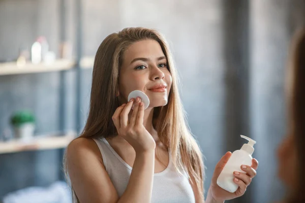 Cuidado com a pele. Mulher milenar bonita removendo maquiagem de seu rosto perto do espelho em casa — Fotografia de Stock