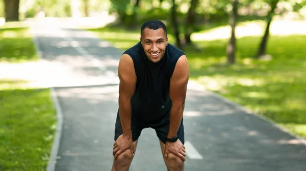 Sorrindo corredor preto descansando após a maratona correr no parque ensolarado — Fotografia de Stock