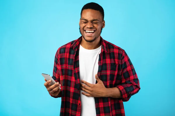 Positivo uomo afroamericano che ride tenendo lo smartphone in piedi in studio — Foto Stock